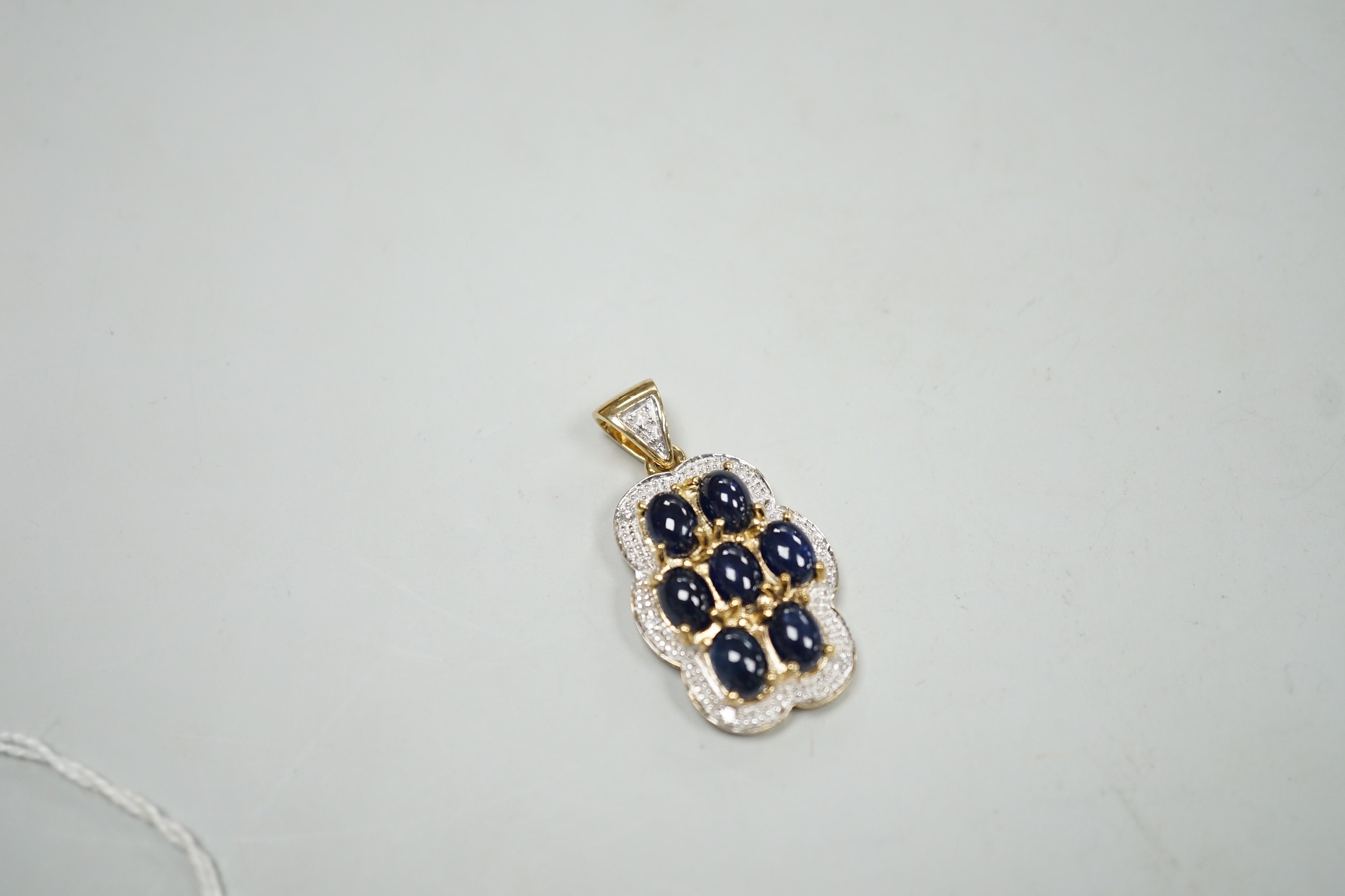 A modern 9ct gold, cabochon sapphire cluster and diamond chip set shaped oval pendant, overall 37mm, gross weight 8.4 grams.